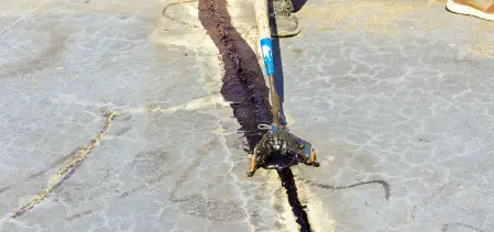 A worker using hot rubber crack filling to repair a large crack in pavement